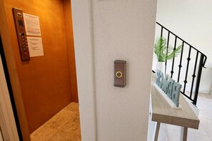 A hallway with an elevator, a call button, and a staircase with a railing. - 6 Bedroom | 7 King Beds | Elevator | Beachfront (Navarre)