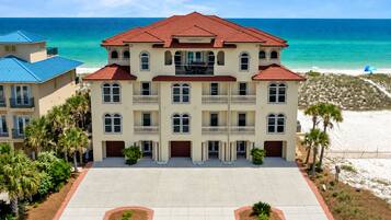 A multi-story hotel with a red-tiled roof, located near a beach with clear blue waters.