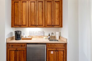 A kitchen with wooden cabinets, a stainless steel dishwasher, a coffee maker, and a sink. - 6 Bedroom | 7 King Beds | Elevator | Beachfront (Navarre)