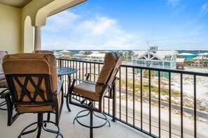 A balcony with two chairs and a table, overlooking a beach and buildings. - 6 Bedroom | 7 King Beds | Elevator | Beachfront (Navarre)