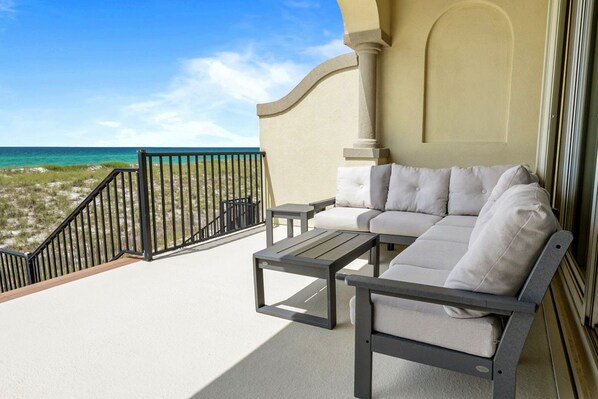 A balcony with a sofa and a table, overlooking a beach. - 6 Bedroom | 7 King Beds | Elevator | Beachfront (Navarre)