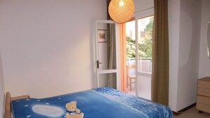 A bedroom with a bed covered in a blue blanket with a bear design, a wooden chair, a dresser, and a view of a balcony with a railing.