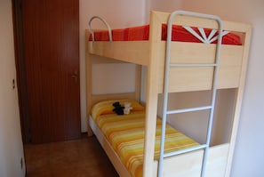 Una cama litera con escalera, una puerta de madera y una colcha a rayas.