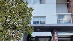 A modern building with a white facade, a black gate, and a tree in front.