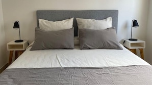 A neatly made bed with a grey headboard, two bedside tables with lamps, and a grey bedspread.