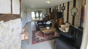 A living room with a fireplace, a television, and a dining area with a table and chairs. - Gites de Charme au Cœur du Perigord Pourpre (Saint-Remy)