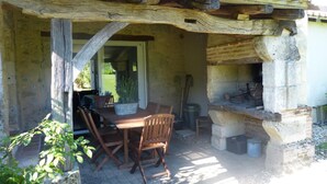 A rustic outdoor patio with a wooden table and chairs, a stone fireplace, and a garden view. - Gites de Charme au Cœur du Perigord Pourpre (Saint-Remy)