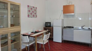 Cozinha compacta com área de refeições, geladeira, fogão e televisão.