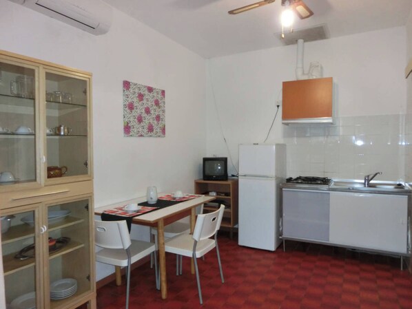 A compact kitchen with a dining area, a refrigerator, a stove, and a television.