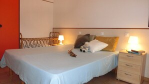 A single bed with a white bedspread, a wooden headboard, two bedside lamps, a nightstand with drawers, and a small figurine on the bed. - Villa in a quiet area next to the sea (Bibione)