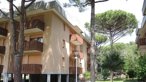 A multi-story residential building with balconies, surrounded by trees and a well-maintained lawn. - Relaxing stay by sea and pines (Bibione)