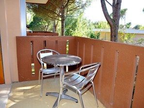 Un balcon avec une table en métal et deux chaises, une clôture marron et des arbres en arrière-plan.