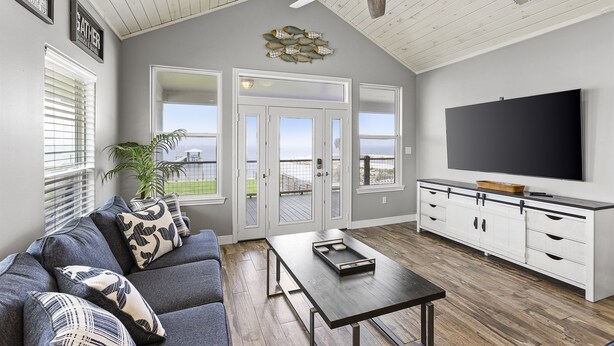 A modern living room with a gray sofa, a coffee table, and a TV on a white cabinet. - Cozy Bay House w/ Heated Spool + Pier (San Leon)