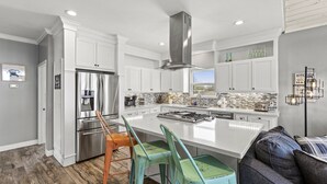 A modern kitchen with white cabinetry, a stainless steel range, and a large island with bar stools. - Cozy Bay House w/ Heated Spool + Pier (San Leon)