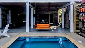 A modern outdoor pool area with a hanging chair, seating, and a covered patio. - Cozy Bay House w/ Heated Spool + Pier (San Leon)