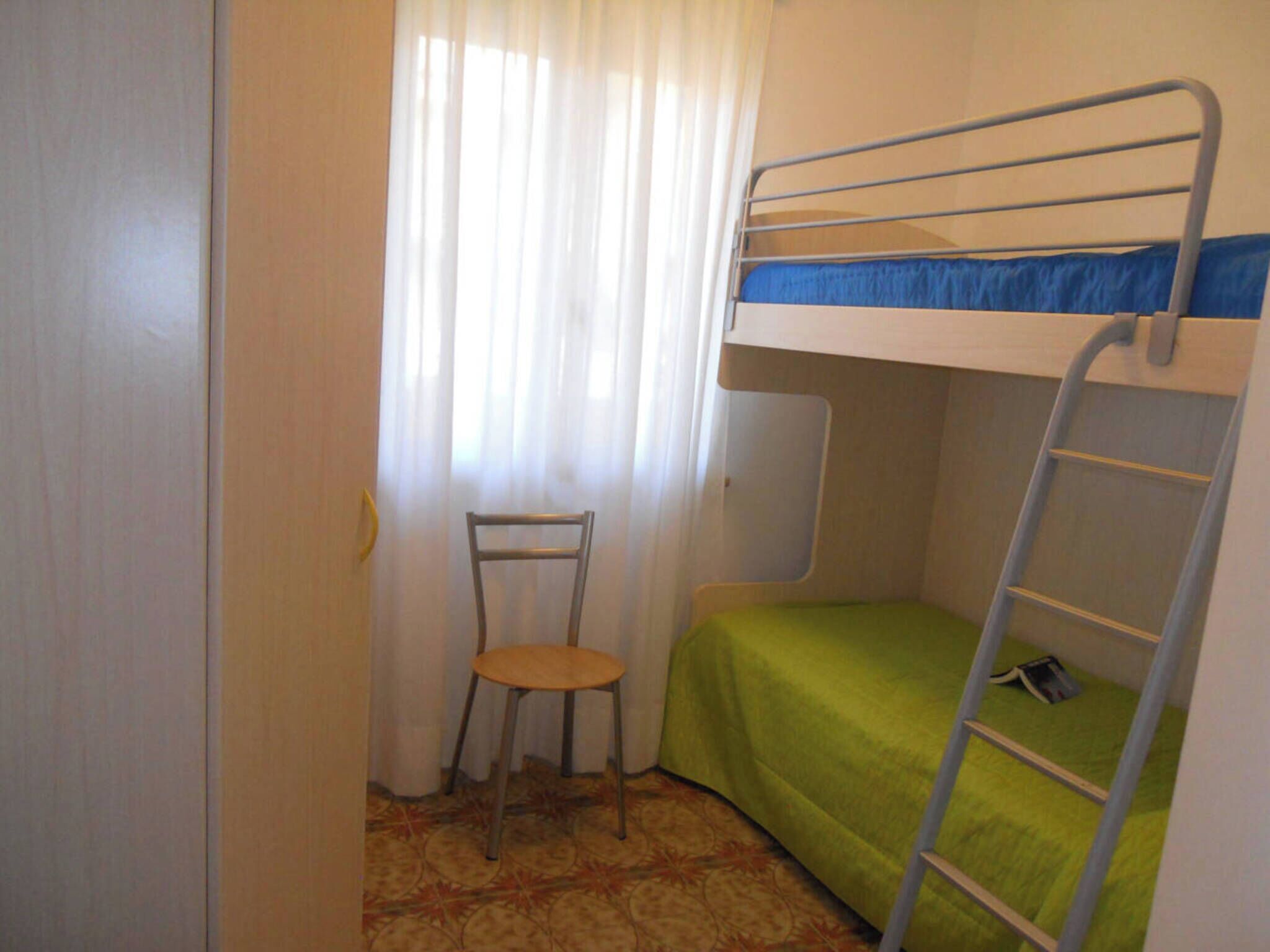 Ein kleines Zimmer mit einem Etagenbett, einem Stuhl und einer Klapptreppe.
