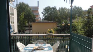 Un balcon avec une table et des chaises, une balustrade et une vue sur des immeubles et des arbres.