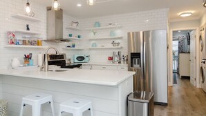 Une cuisine moderne avec des meubles blancs, des appareils en acier inoxydable et des luminaires suspendus.