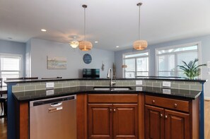 A kitchen with a curved island, wooden cabinets, a dishwasher, and pendant lighting.