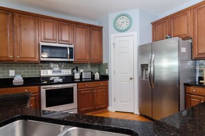 A kitchen with wooden cabinets, a stainless steel refrigerator, a microwave, and an oven. - Get caught up in "Riptide" (Carolina Beach)