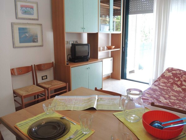 A small room with a dining table set for two, a television, and a window with a view of the outside. - One-bedroom flat next to Bibione Thermae (Bibione)
