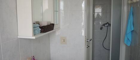 A bathroom with a white sink, a mirror above it, a shower area with a glass door, and a towel hanging on the wall.