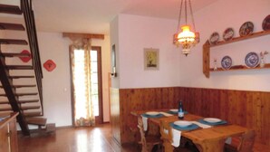 A dining area with a wooden table and chairs, a staircase, and a wall-mounted shelf with plates.