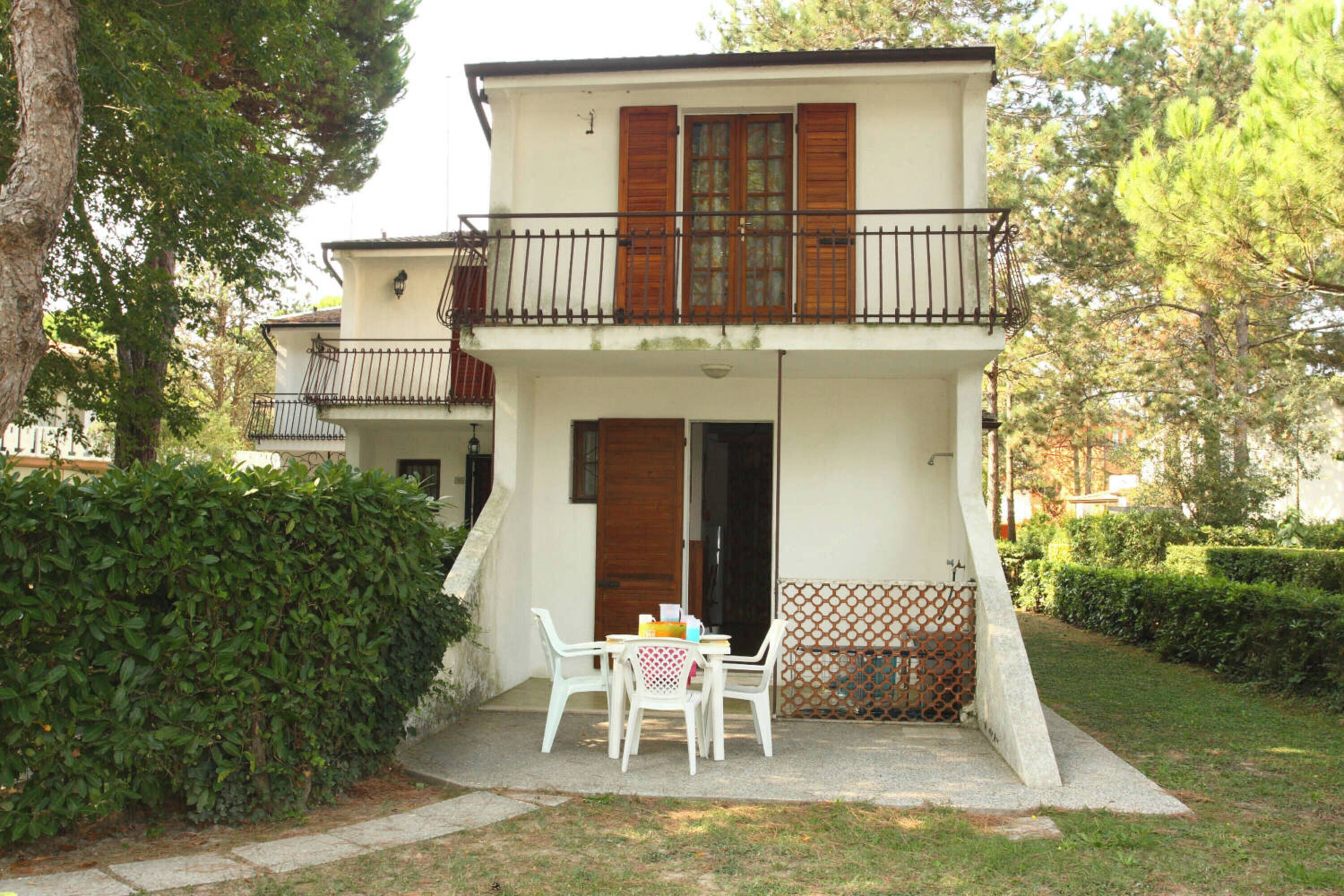 Un bâtiment à deux étages doté d’un balcon, d’une table avec des chaises et d’un arbuste en premier plan.