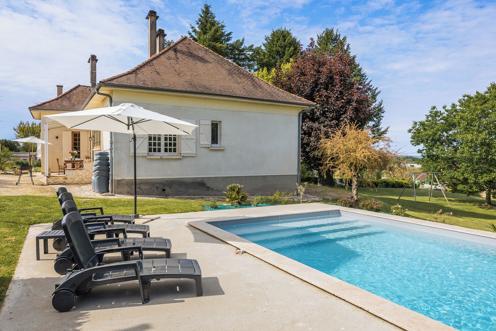 Ein Swimmingpool mit Liegestühlen, einem Sonnenschirm und einem Haus im Hintergrund.