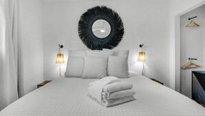 A modern bedroom with a large bed, two bedside lamps, a round mirror, and a wall-mounted coat rack.