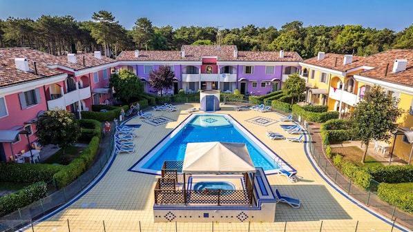 A resort with a central swimming pool, sun loungers, and a covered area.