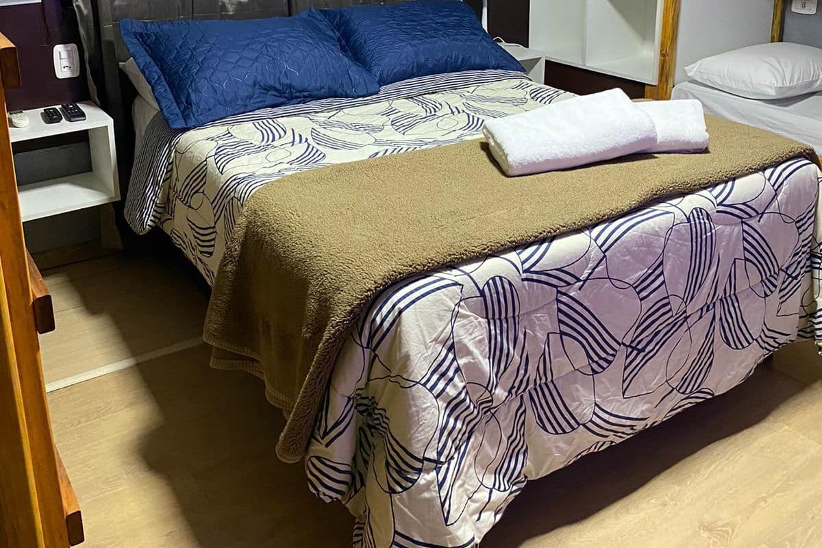 Ein Hotelzimmer mit Bett, Nachttisch, Lampe, Kleiderschrank und einem Fenster mit Vorhängen.