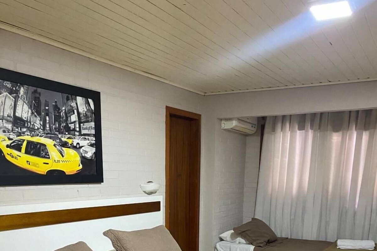 Ein Hotelzimmer mit Bett, Nachttisch, Lampe, einem Gemälde und einem Fenster mit Vorhängen.