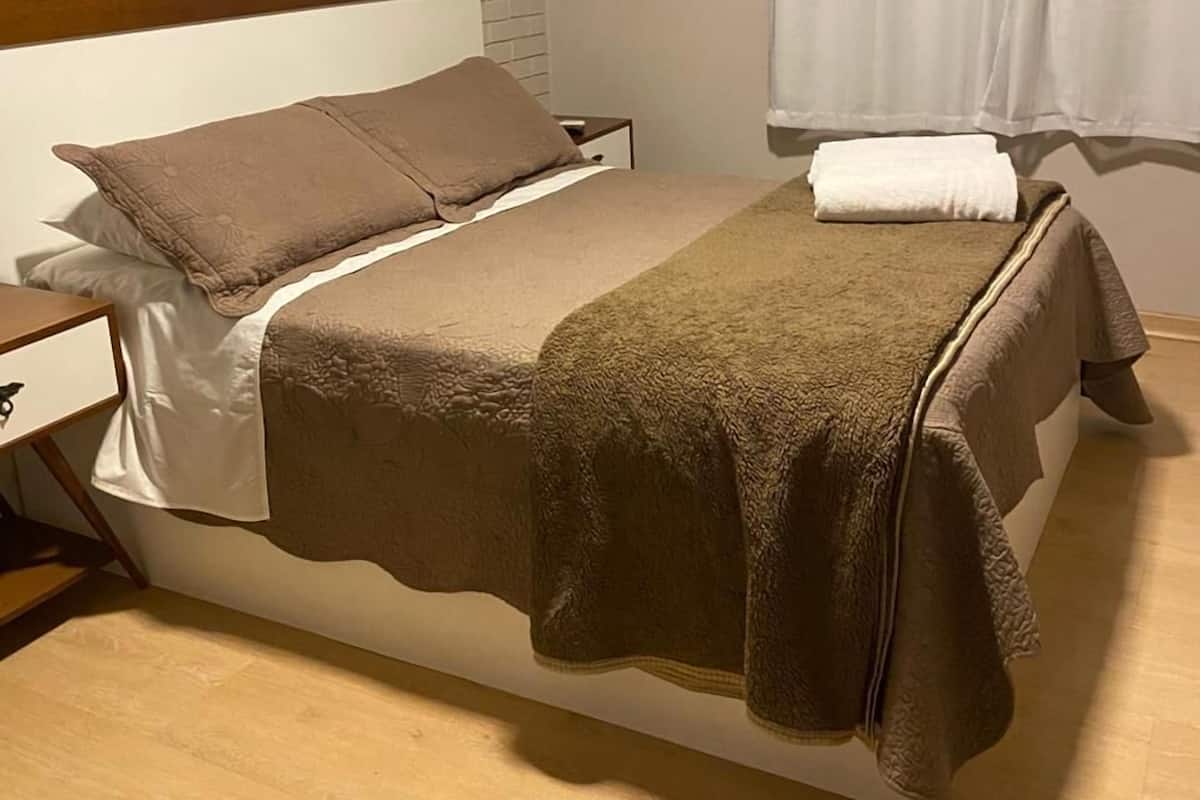 Ein Hotelzimmer mit Bett, Nachttisch, Wand-Klimaanlage, einem Bild und einem Fenster mit Vorhängen.