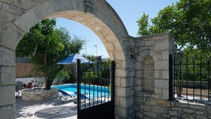 Un arco in pietra conduce a una zona piscina con lettini e un ombrellone blu.