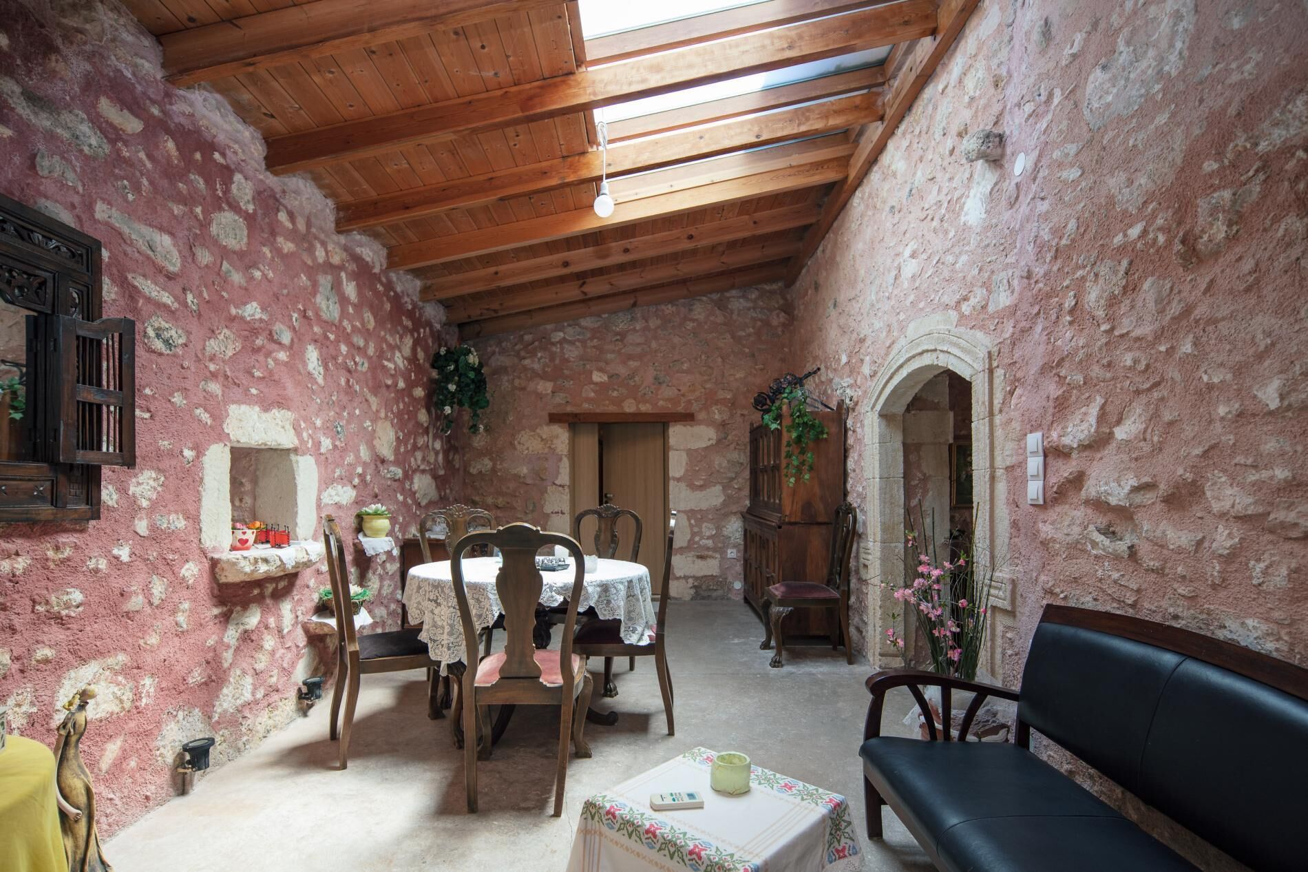 A rustic dining area with a wooden ceiling, stone walls, a round table with chairs, and a bench.