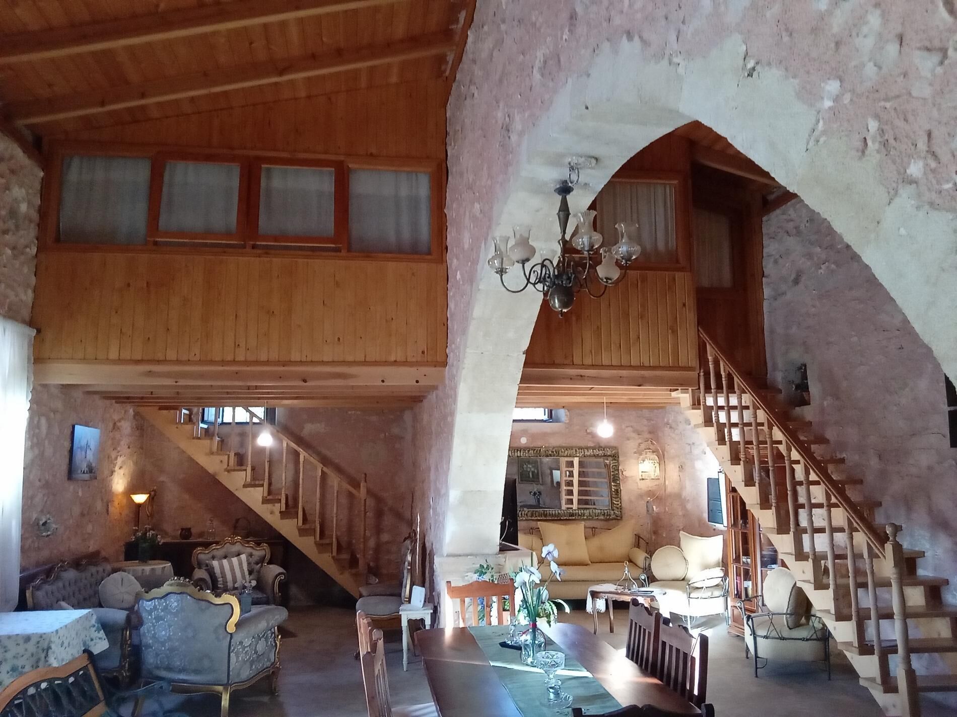 A spacious loft-style room with a high ceiling, wooden beams, a staircase, and a dining area.