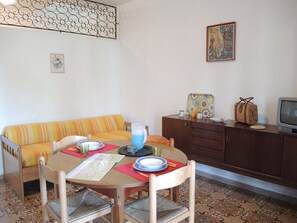 Un comedor con una mesa dispuesta para dos, un sofá, un armario y un televisor.