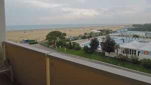 A view from a balcony overlooking a beach with a pool area and buildings in the foreground. - Adorable flat with large terrace overlooking the sea (Bibione)