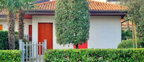 A residential building with a red door, a small garden, and a metal gate.