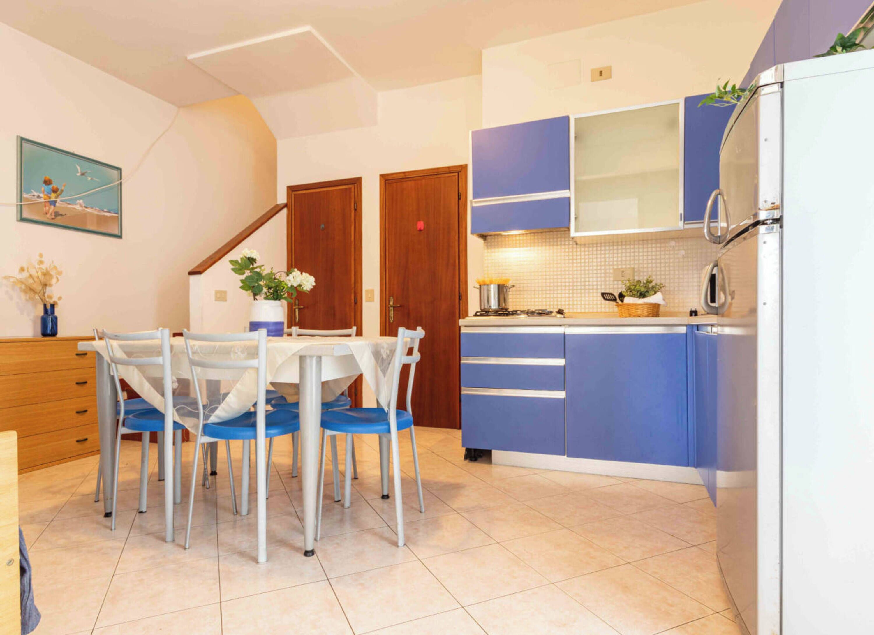 A kitchen with a dining table, chairs, cabinets, and a refrigerator.