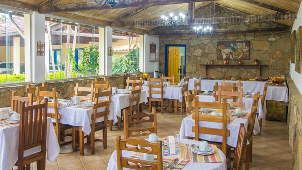 Un restaurante con mesas y sillas de madera, paredes de piedra y vistas al exterior con vegetación.