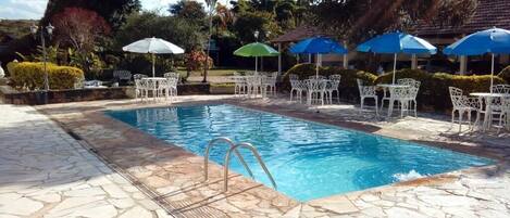 Una piscina rectangular con una terraza de losas de piedra, rodeada de sillas blancas y sombrillas azules.