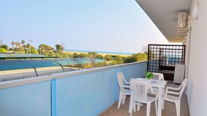 Een balkon met een tafel en stoelen, met uitzicht op een zwembad en strand.
