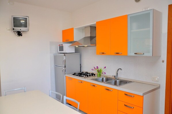 A compact kitchen with orange cabinets, a microwave, a gas stove, and a small sink.