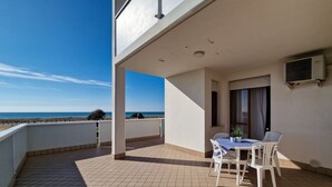 A balcony with a view of the sea, a table with chairs, and an air conditioning unit on the wall. - Cozy studio with side sea view in Bibione (Bibione)