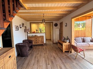 Un'ampia zona giorno con soffitto in legno, un divano, un tavolo da pranzo e una cucina sullo sfondo.