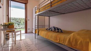 Habitación tipo dormitorio con literas, una pequeña mesa con silla y una planta en maceta.