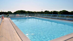 Una piscina rectangular con borde de baldosas, rodeada por una cerca azul y árboles al fondo.