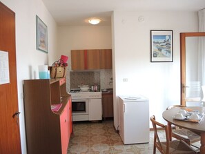 Une cuisine compacte équipée d’un réfrigérateur, d’un four et d’un four à micro-ondes. On y trouve une table à manger avec des chaises et une fenêtre donnant sur un paysage agréable.
